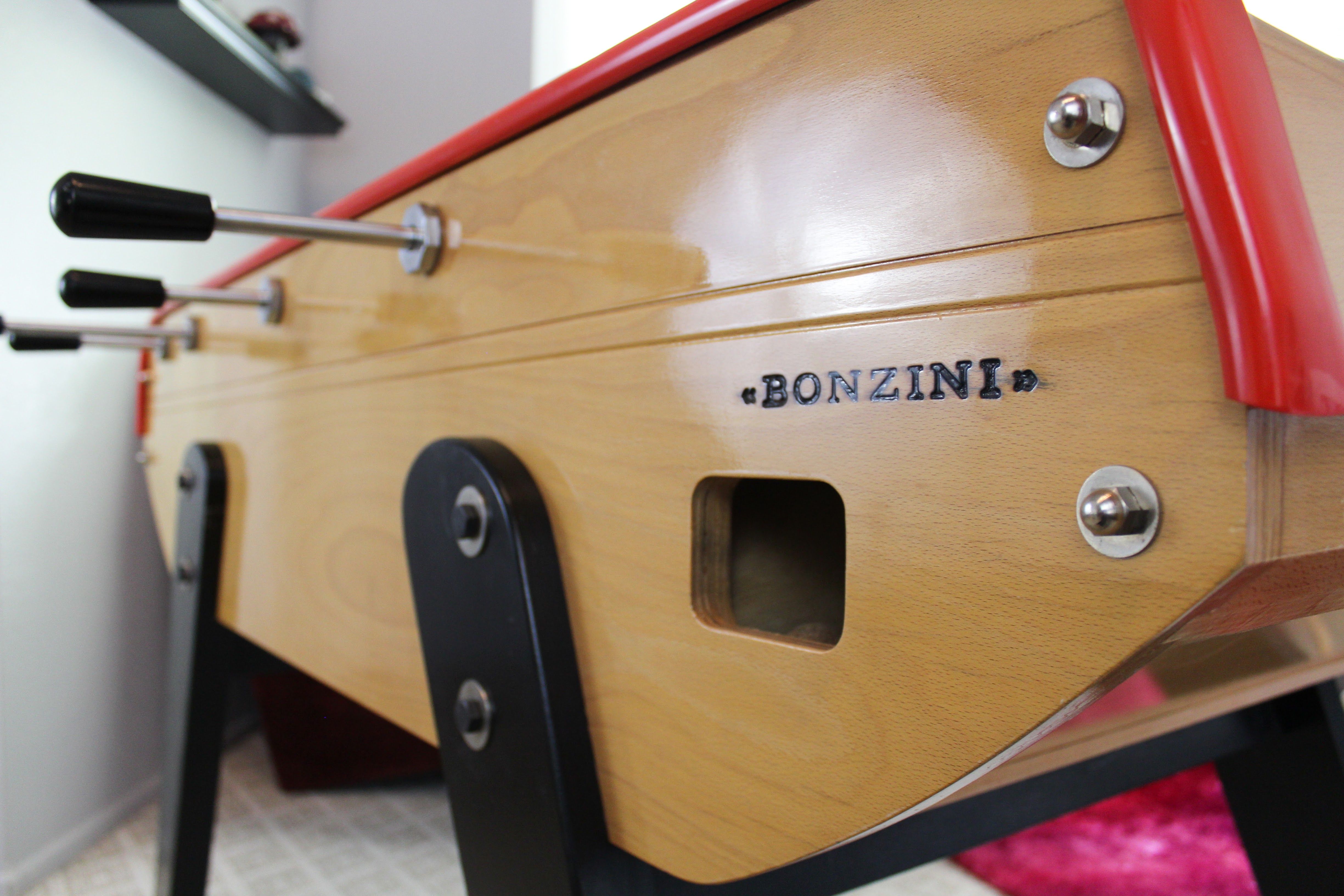 A Bonzini foosball table with a wood cabinet and red trim highlights craftsmanship and precise hardware details.